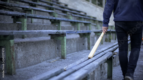 Foto Young man walking on stadium tribune with baseball bat, youth gang, vandalism