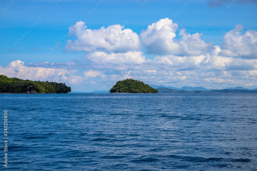 Blue sea and sky landscape with distant tropical island. Tropical cloudscape with green island photo background.