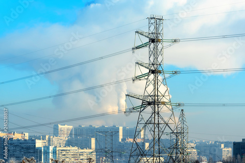 Metal supports of the high-voltage power line in front, against the background, in a frosty haze, residential high-rise buildings and Smoking pipes. A lot of snow.