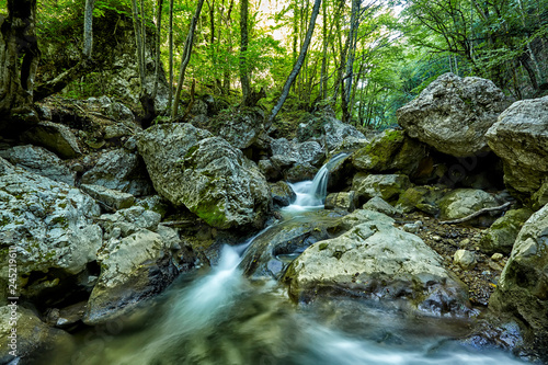 Beautiful waterfall in autumn forest in crimean mountains. Stones with moss in the water. Blurred water.