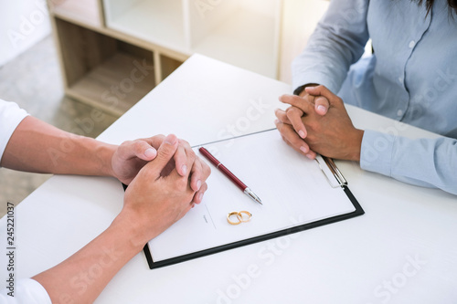 Husband and wife are reading divorce agreement and signing decree of divorce (dissolution or cancellation) of marriage filing divorce papers and two golden marry ring photo