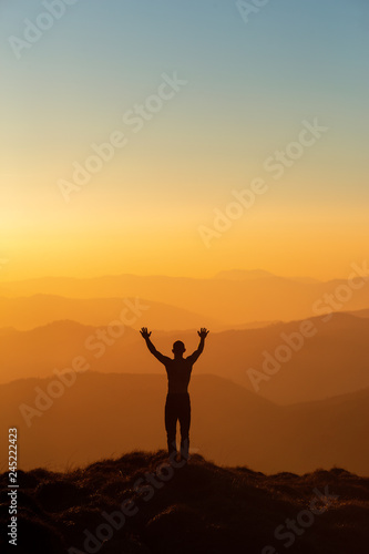 Man silhouette standing with hands up achieving the top. Hiker welcomes a sun. Tourist open arms on sunrise mountain top