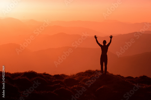 Man silhouette standing with hands up achieving the top. Hiker welcomes a sun. Tourist open arms on sunrise mountain top