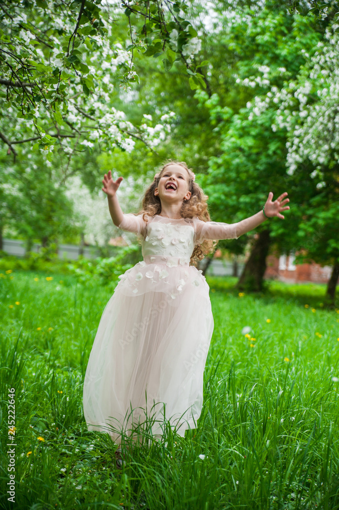 Little beautiful girl in a smart white dress in blooming apple blossom garden.