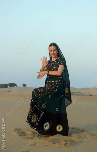 A young woman in Indian national dress, lit by the setting sun, dancing in the sands of the Thar desert. Rajasthan, India.