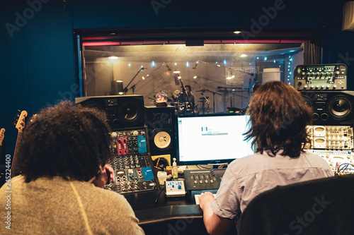 Music Engineer and Artist in Music Recording studio at mixing consol recording hip hop music viewing artists through glass