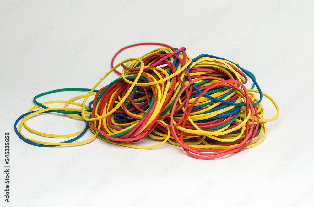 A pile of multi-colored rubber bands stationery, ready to use, is disordered mass on a white plane, close-up. A pile of multi-colored rubber bands stationery, ready to use, is disordered mass on a white plane, close-up.