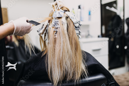 Hairdresser is dying female hair, making hair highlights to his client with a foil.