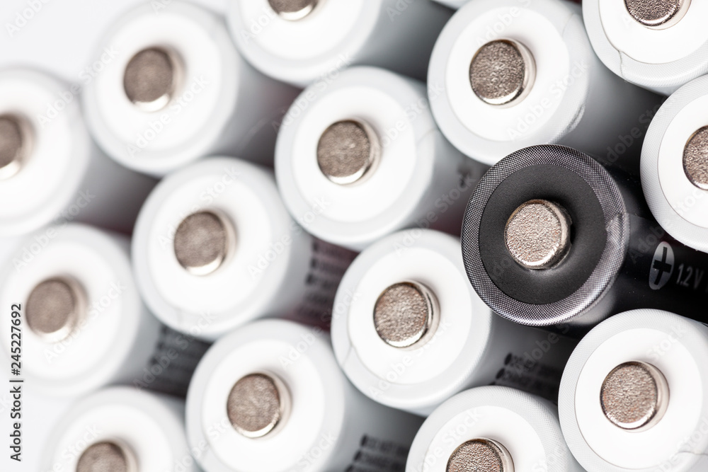 AA batteries are located close to each other. Close-up of all white batteries, except one black, on a white background. Battery technology AA batteries are located close to each other. Close-up of all white batteries, except one black, on a white background. Battery technology