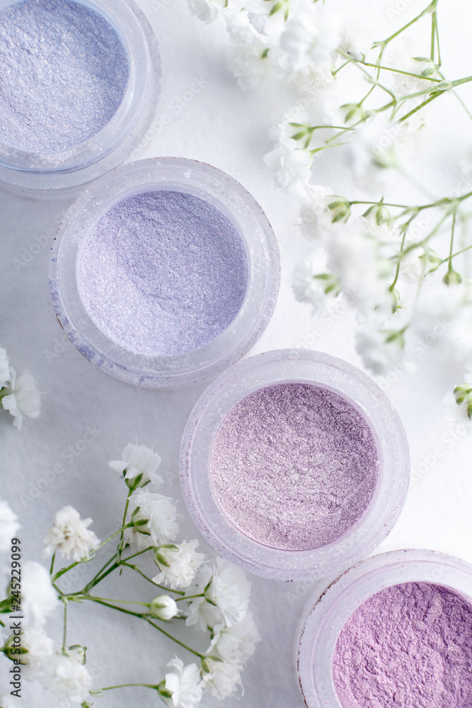 Fototapeta flat lay jars of eye shadow in pastel spring colors on a white textured background with delicate white flowers gypsophila