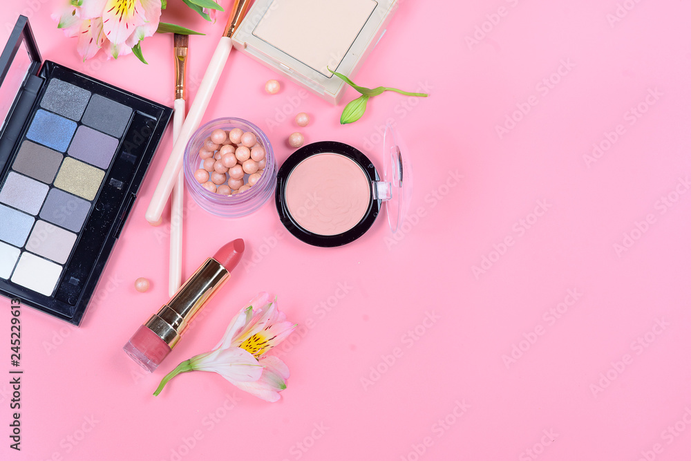 Fototapeta premium Makeup cosmetics and flowers on pink background. Top view.