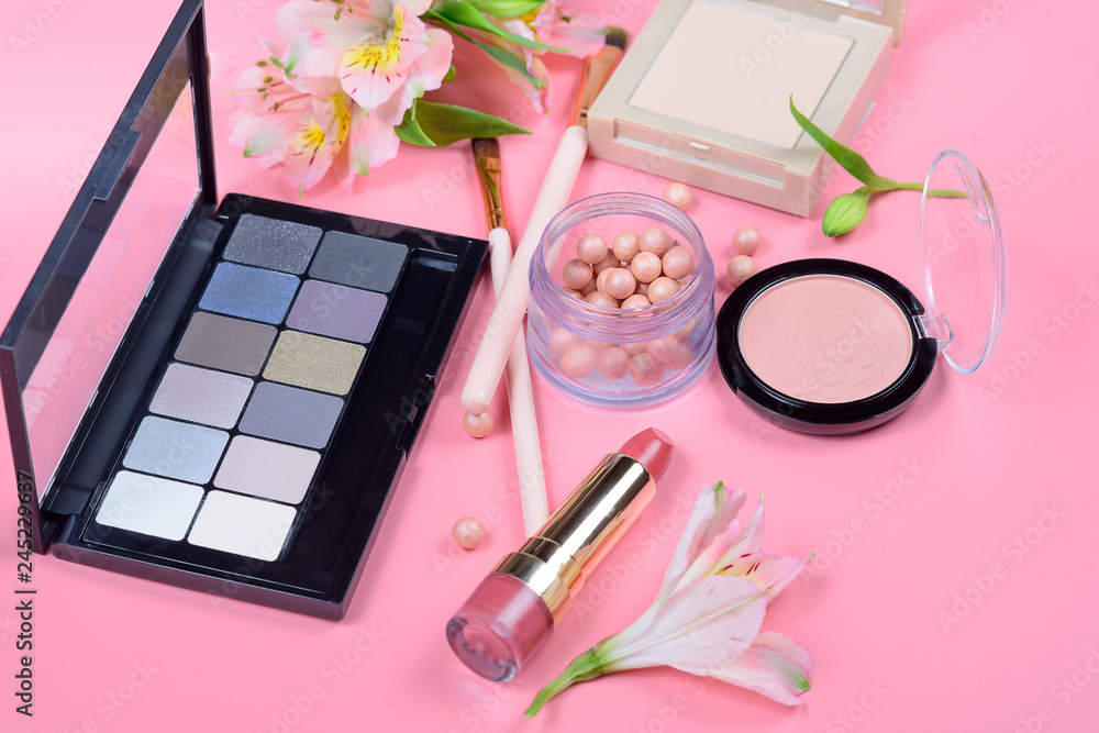 Fototapeta premium Makeup cosmetics and flowers on pink background. Top view.