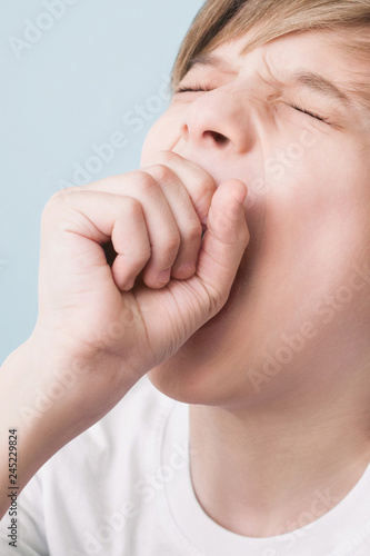 Boy yawns wide with his eyes closed, covering his mouth with his fist