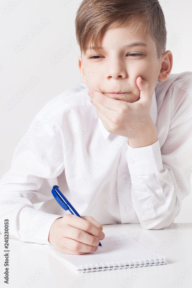 Pensive school boy writes in notebook at the table Pensive school boy writes in notebook at the table