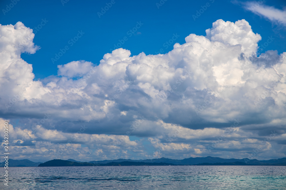 Blue sea and sky landscape with distant island. Romantic tropical cloudscape with green island photo background. Blue sea and sky landscape with distant island. Romantic tropical cloudscape with green island photo background.