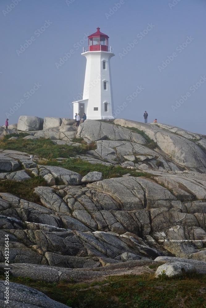 Peggy’s Cove, Nova Scotia, Canada: Visitors tour the picturesque Peggy’s Point Lighthouse (1914) shrouded in morning mist.