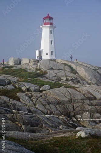 Peggy’s Cove, Nova Scotia, Canada: Visitors tour the picturesque Peggy’s Point Lighthouse (1914) shrouded in morning mist.