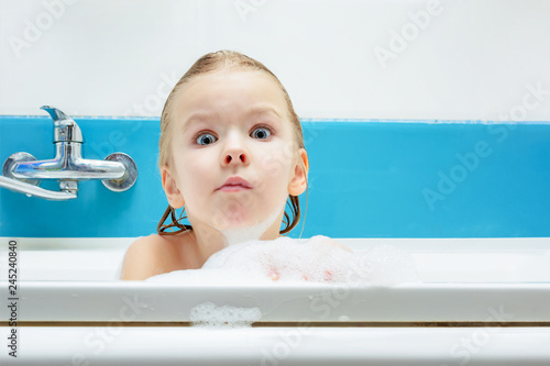Beautiful, little girl taking a bath with foam. The child looks at the camera in surprise.