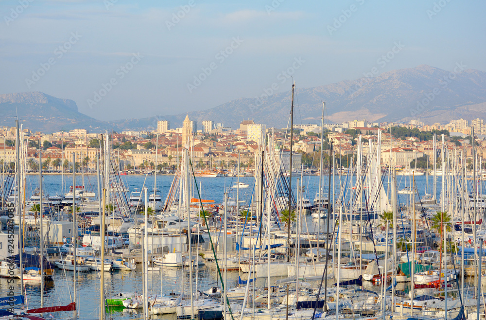 View of many parked yachts and boats in the bay of Split City downtown centre, as well as waterfront with tour and fisher boats. Evening.