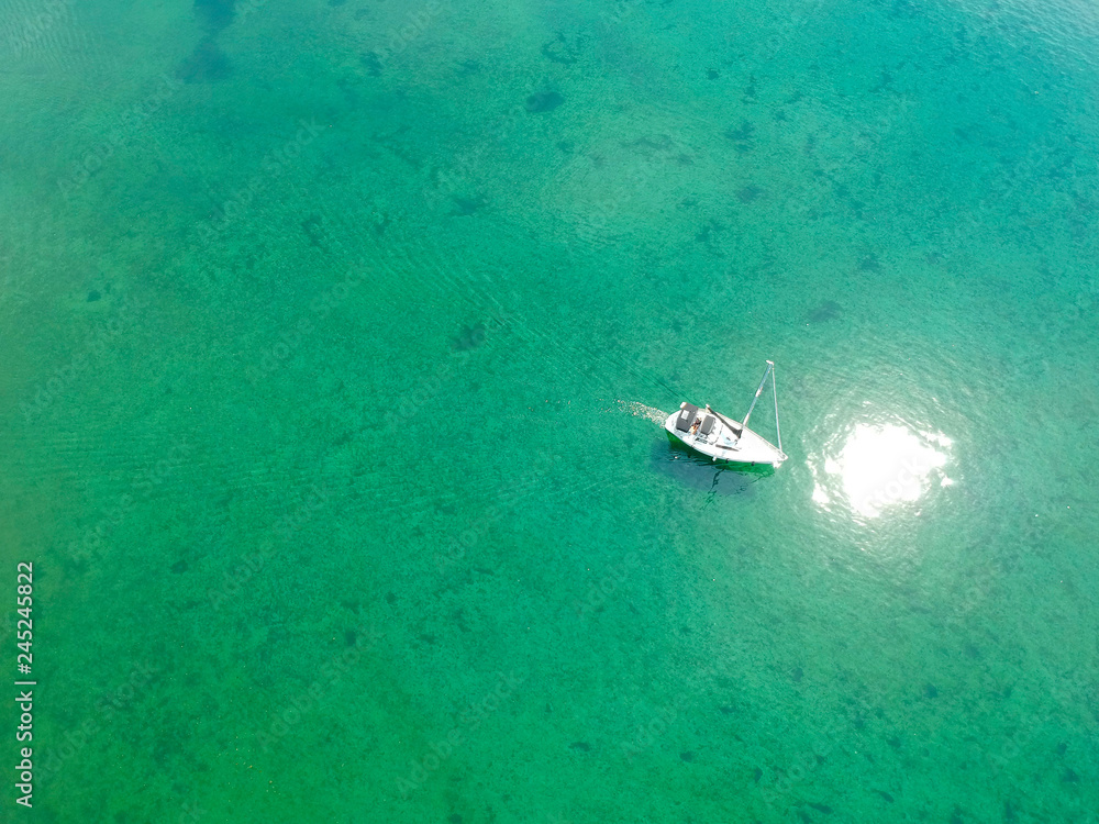 Aerial view of a beautiful boat sailing on a transparent calm and turquoise Mediterranean sea water.