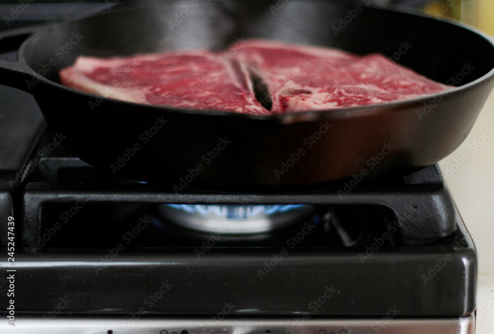 New York strip steaks cooking in a cast iron pan on a natural gas stove top.
New York strip steaks cooking in a cast iron pan on a natural gas stove top.