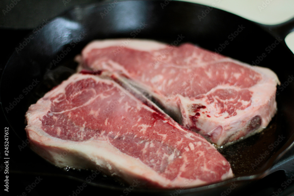 New York strip steaks cooking in a cast iron pan on a natural gas stove top.
New York strip steaks cooking in a cast iron pan on a natural gas stove top.
