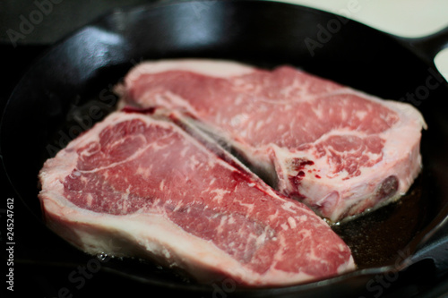 New York strip steaks cooking in a cast iron pan on a natural gas stove top. 