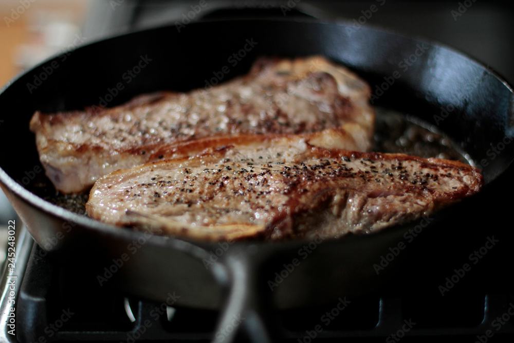 New York strip steaks frying in a cast iron pan on a natural gas stove top. New York strip steaks frying in a cast iron pan on a natural gas stove top.