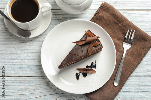 Slice of tasty chocolate cake and cup of coffee served on wooden table, top view