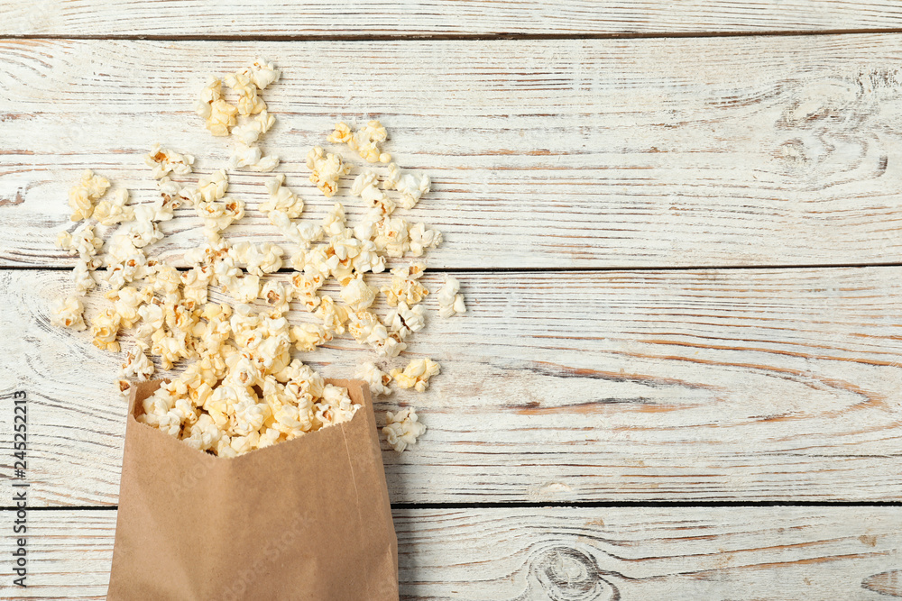 Overturned paper bag with popcorn on white wooden background, top view. Space for text Overturned paper bag with popcorn on white wooden background, top view. Space for text