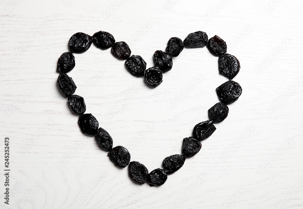 Heart shaped frame of sweet dried plums on wooden background, top view with space for text. Healthy fruit Heart shaped frame of sweet dried plums on wooden background, top view with space for text. Healthy fruit
