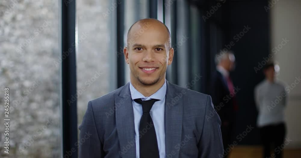 4K Portrait of handsome businessman looking directly at camera & smiling, with colleagues talking in background. Slow motion. 4K Portrait of handsome businessman looking directly at camera & smiling, with colleagues talking in background. Slow motion.