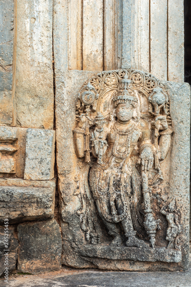 Belavadi, Karnataka, India - November 2, 2013: Veera Narayana Temple. Closeup of Brown stone Sculpture of Lord Vishnu set against wall outside entry hall to sanctuary . Partly damaged.