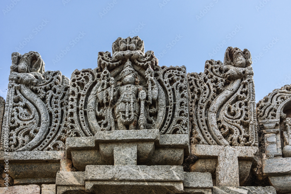 Belavadi, Karnataka, India - November 2, 2013: Veera Narayana Temple. Vishnu statue on side of One of the three Vimana Towers against blue sky. 