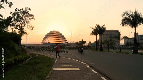 Very wide view of a Kigali roundabout at sunset, cars and people, convention center dome in front of the sun, Rwanda. photo