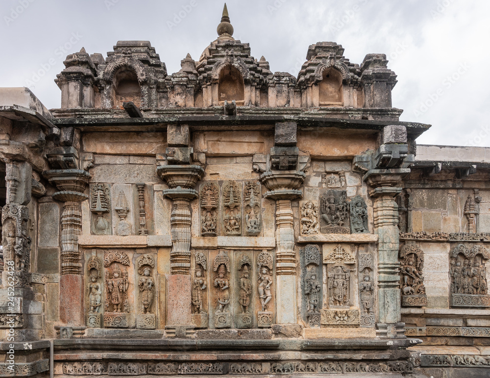 Belur, Karnataka, India - November 2, 2013: Chennakeshava Temple . Large Brown wall stone side panel sculpture of many idols each on their pedestals. White sky.