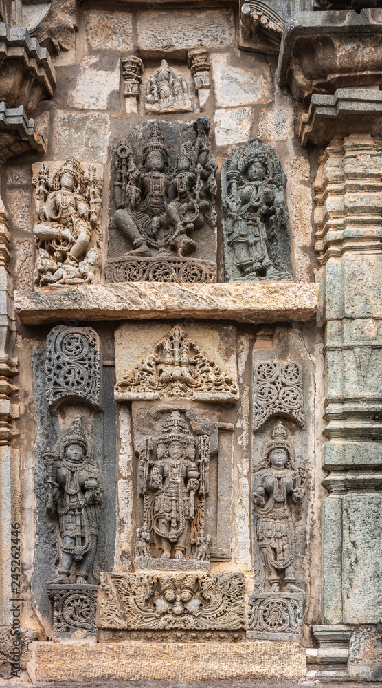 Belur, Karnataka, India - November 2, 2013: Chennakeshava Templ. Large Brown wall stone side panel sculpture of the three main gods each surrouned by their wives and consorts.