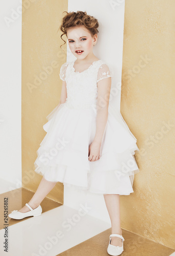 little girl with blond hair wearing white dress.