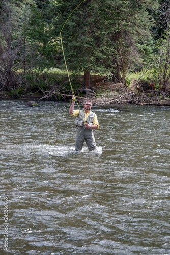 Angler fly fishing in Colorado river wearing gray waders and yellow shirt.