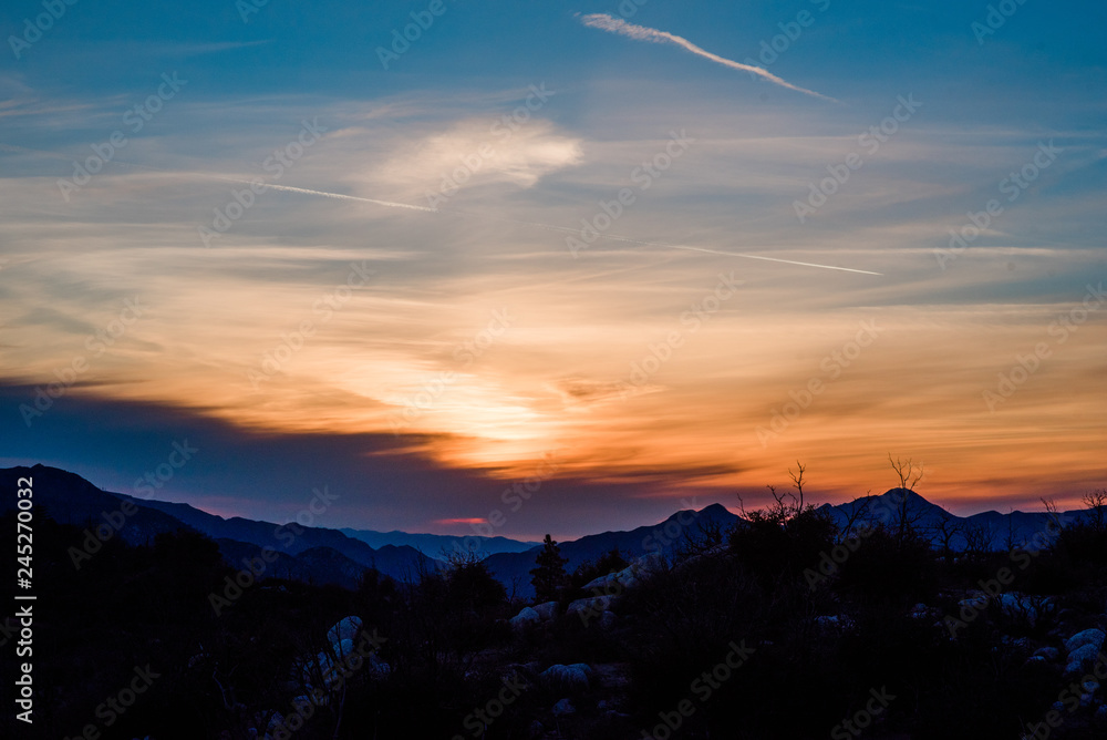 Obraz premium Wispy glowy orange and peach sunset over blue ridges in California mountains