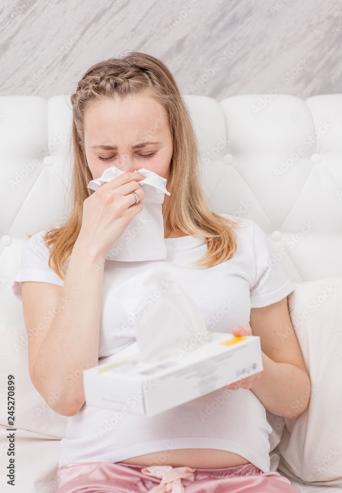 Pregnant woman blowing nose into tissue at home Pregnant woman blowing nose into tissue at home