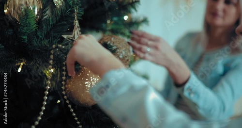 Mom and daughter decorate the Christmas tree. Girl hangs a ball on a branch of spruce. Close-up.