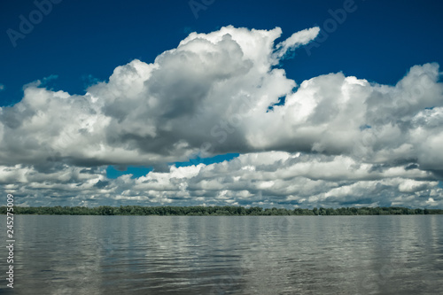 Big white clouds on the blue sky above the river.