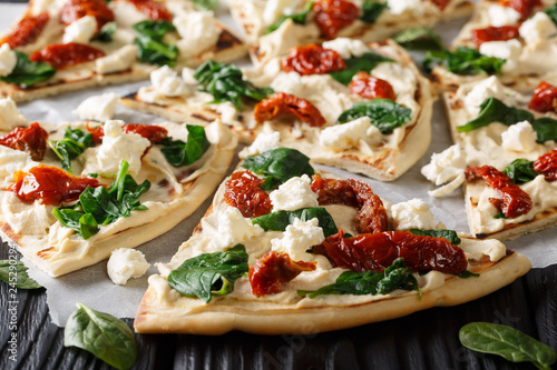 Freshly baked flatbread with hummus, sun-dried tomatoes, spinach and goat cheese close-up. horizontal