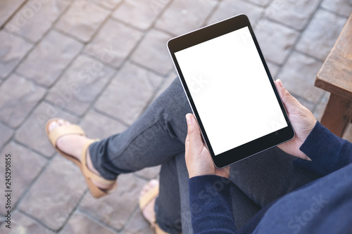 Mockup image of a woman holding black tablet pc with blank white screen while sitting in the outdoors