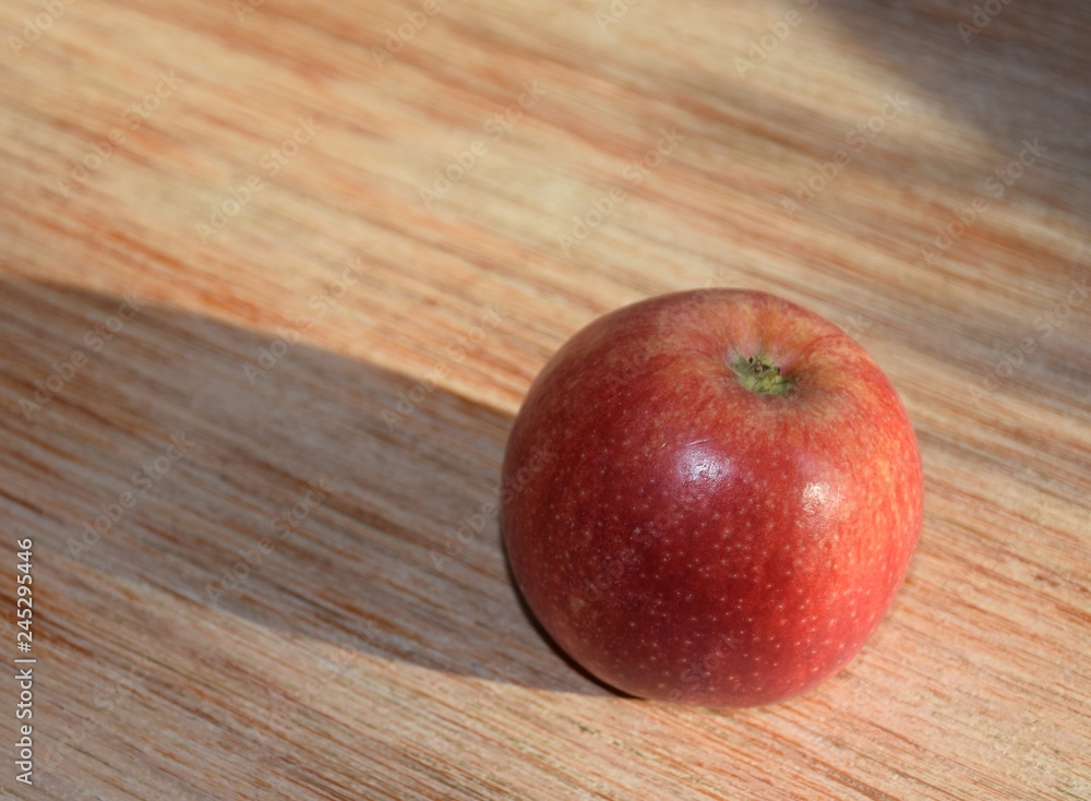 Roter Apfel mit langen Schatten auf einem Holzbrett