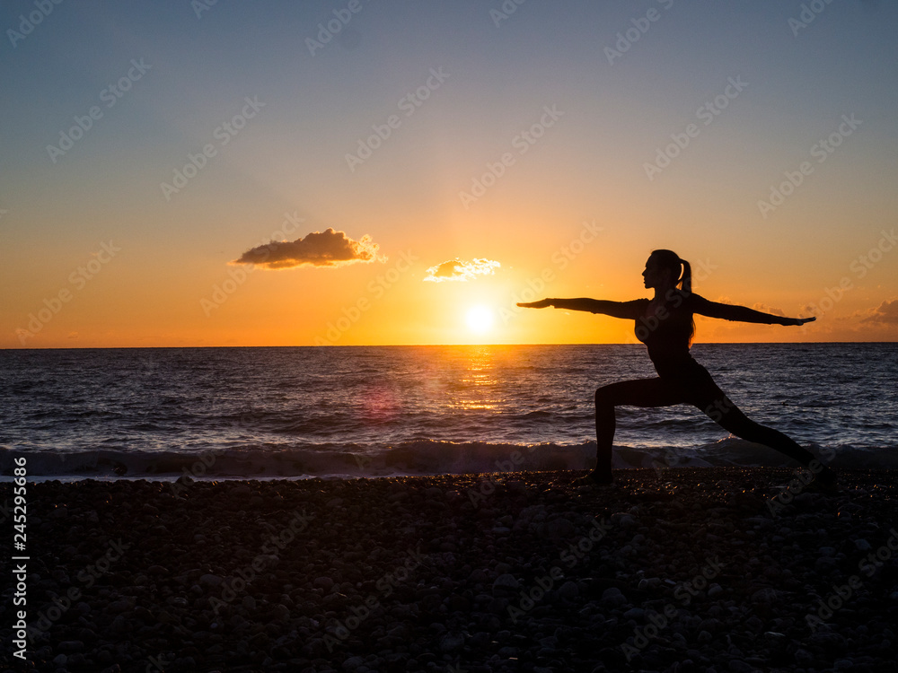 Silhouette woman practicing yoga or stretching on the beach pier at sunset or sunrise. Yoga practice, meditation and healt concept.
