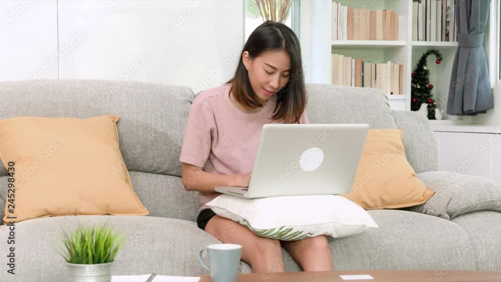 Attractive young asian woman working with notebook computer on light brown sofa in beautigul decoration living room, happy lifestyle concept. Attractive young asian woman working with notebook computer on light brown sofa in beautigul decoration living room, happy lifestyle concept.