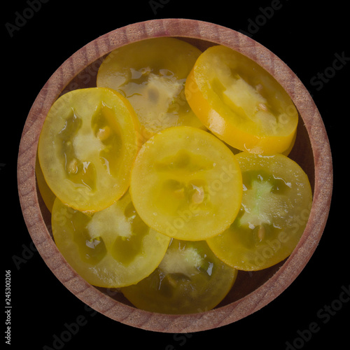 slices of yellow tomatoes  in wooden cup isolated on black background. top view