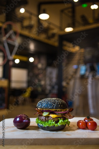An appetizing black hamburger on a wooden board with fresh vegetables.